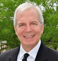 Professional headshot of a smiling older male dental team member in a suit and tie outdoors