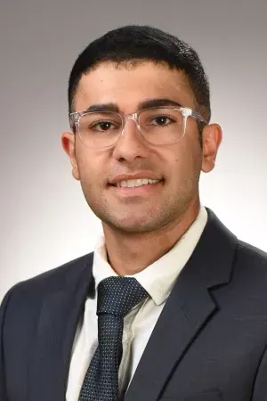 Professional headshot of a male dental team member in glasses, suit jacket, and tie against a light background