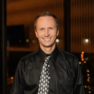 Professional headshot of a smiling male dental team member wearing a dark dress shirt and patterned tie