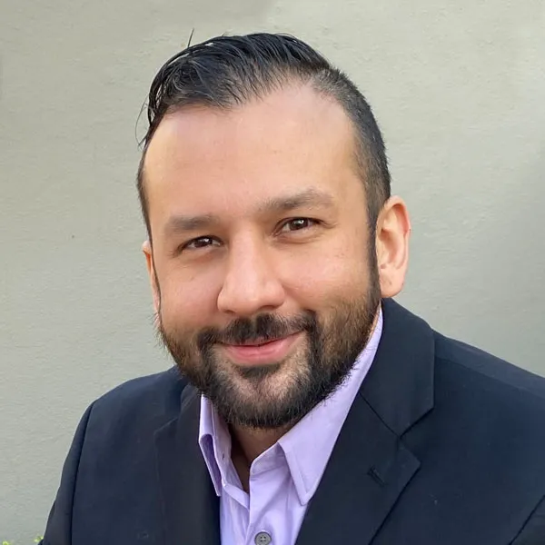 Professional headshot of a bearded male dental team member in a blazer against a light neutral background