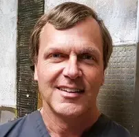 Professional headshot of an older male dental team member against a neutral textured background