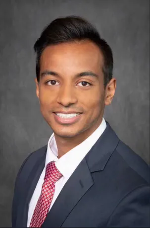 Professional headshot of a smiling male dental provider in a suit and tie against a gray studio background