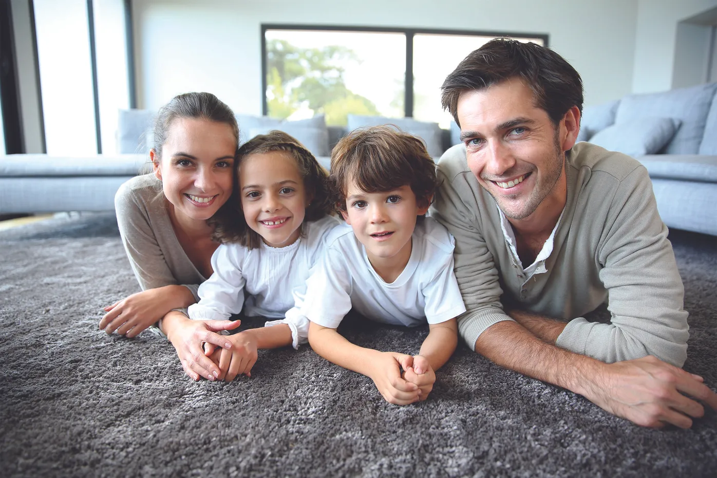 Smiling family portrait with two parents and two children lying together, used for patient-focused dental marketing imagery