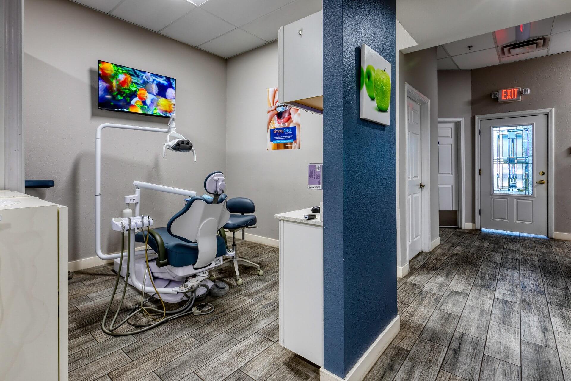 Dental treatment room with patient chair, mounted monitor, partition wall, and clean modern interior finishes