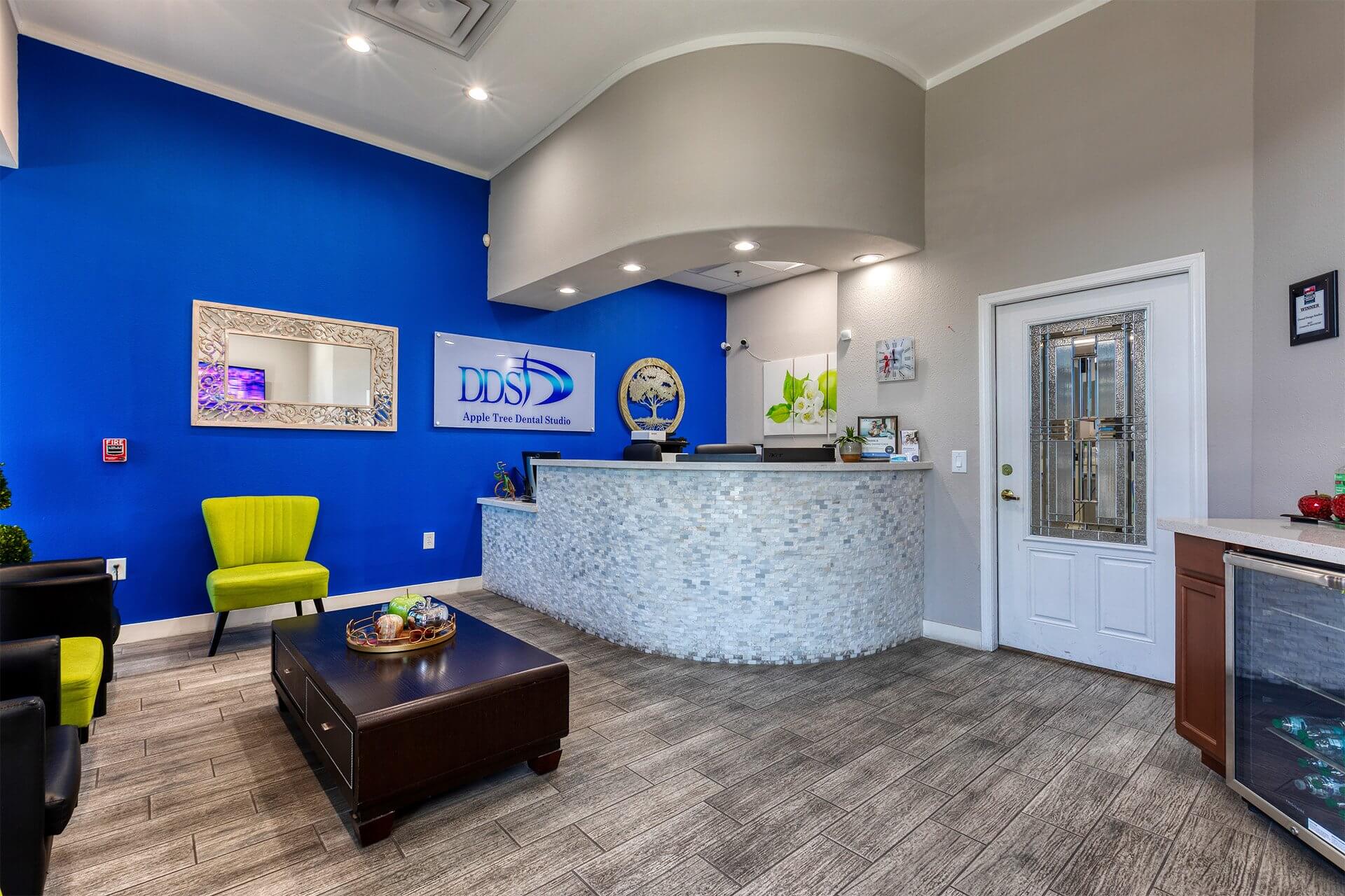 Modern dental reception area with curved front desk, blue accent wall, wood-look flooring, and bright overhead lighting