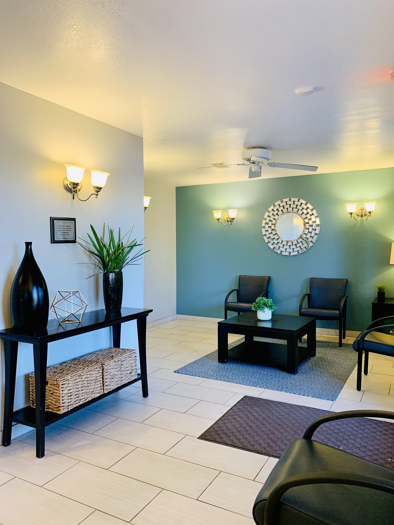 Bright dental office waiting area with teal accent walls, black chairs, framed decor, and a small glass coffee table