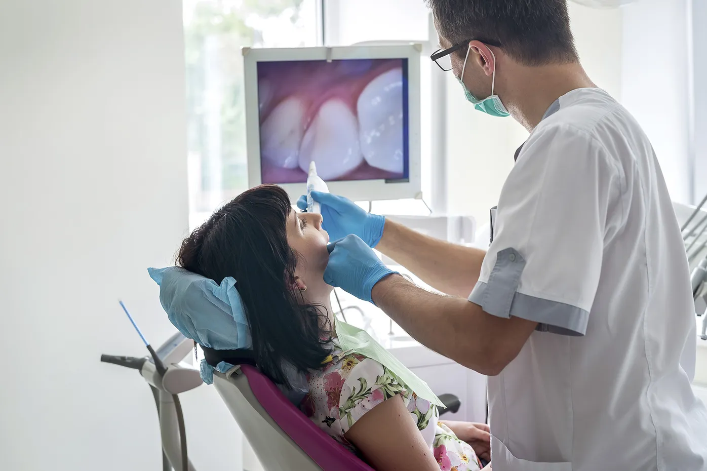 Dentist treating a child patient in a dental operatory while reviewing imaging on a nearby monitor