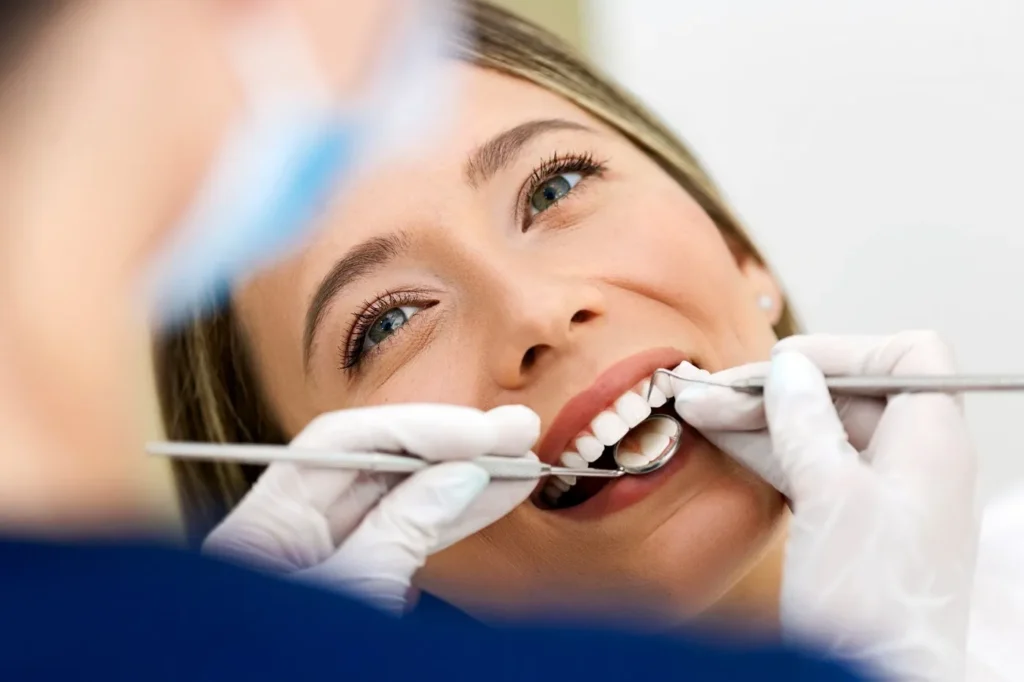Patient receiving an intraoral dental exam while reclining in a treatment chair under bright clinical lighting