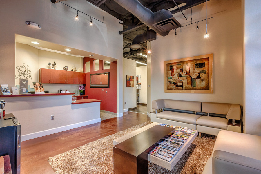 Stylish dental office lobby with red walls, front desk, modern bench seating, exposed ceiling details, and warm lighting