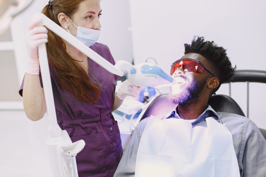 Dental professional performing in-office teeth whitening on a patient with a whitening light