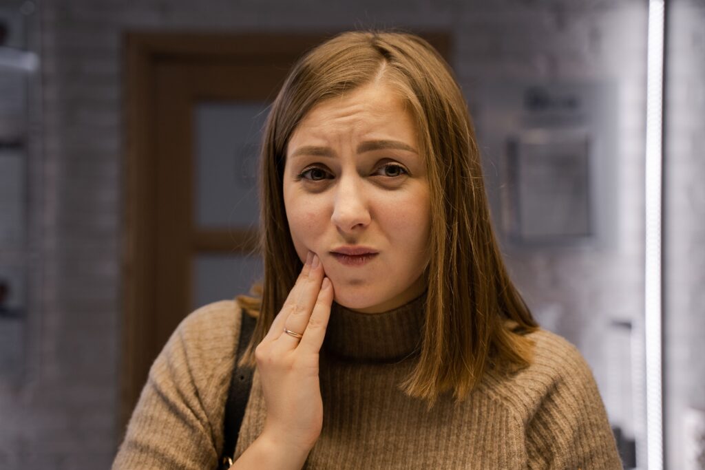 young woman holding her cheek in discomfort at a dental clinic, illustrating possible wisdom tooth pain