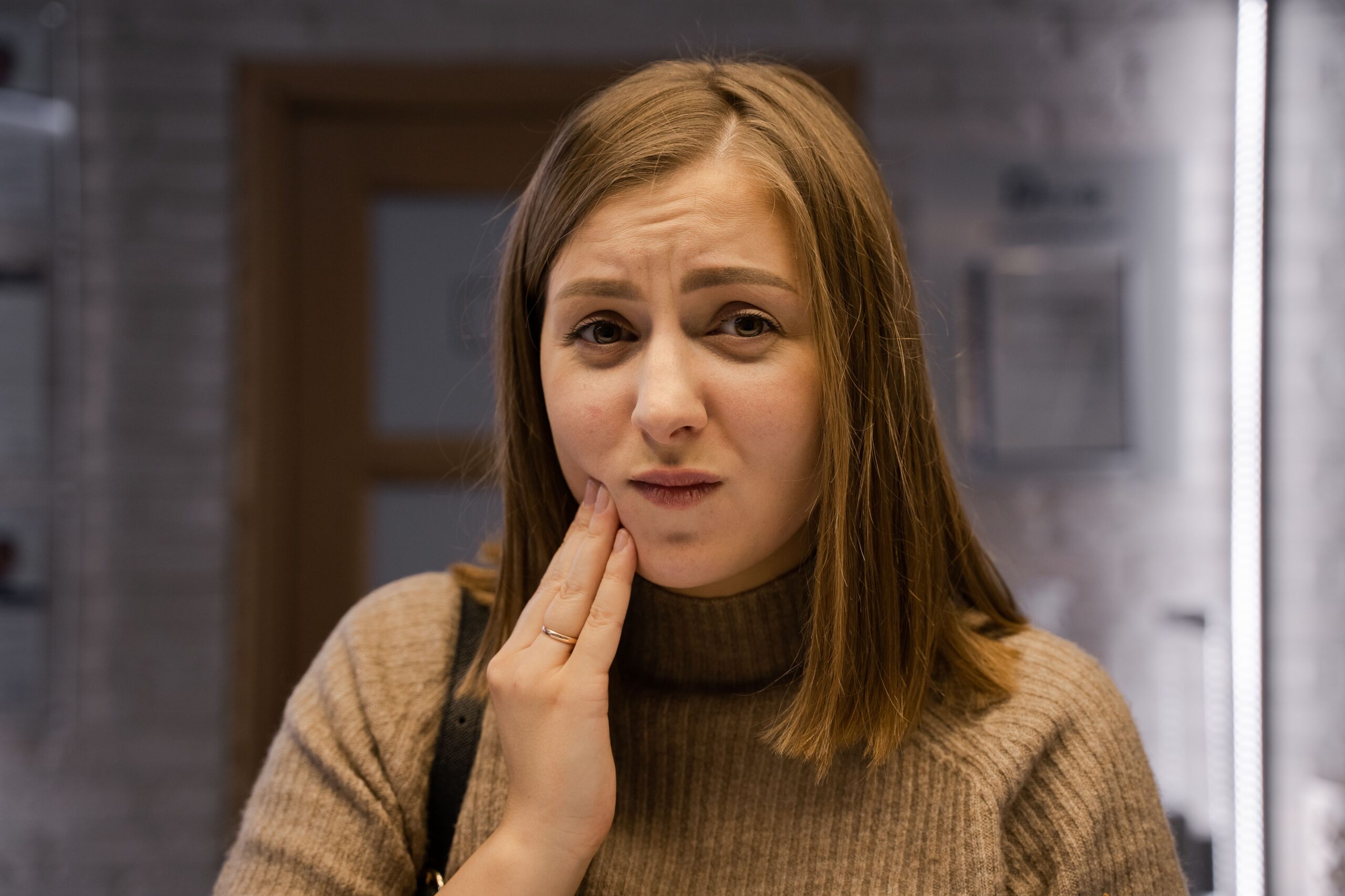 young woman holding her cheek in discomfort at a dental clinic, illustrating possible wisdom tooth pain