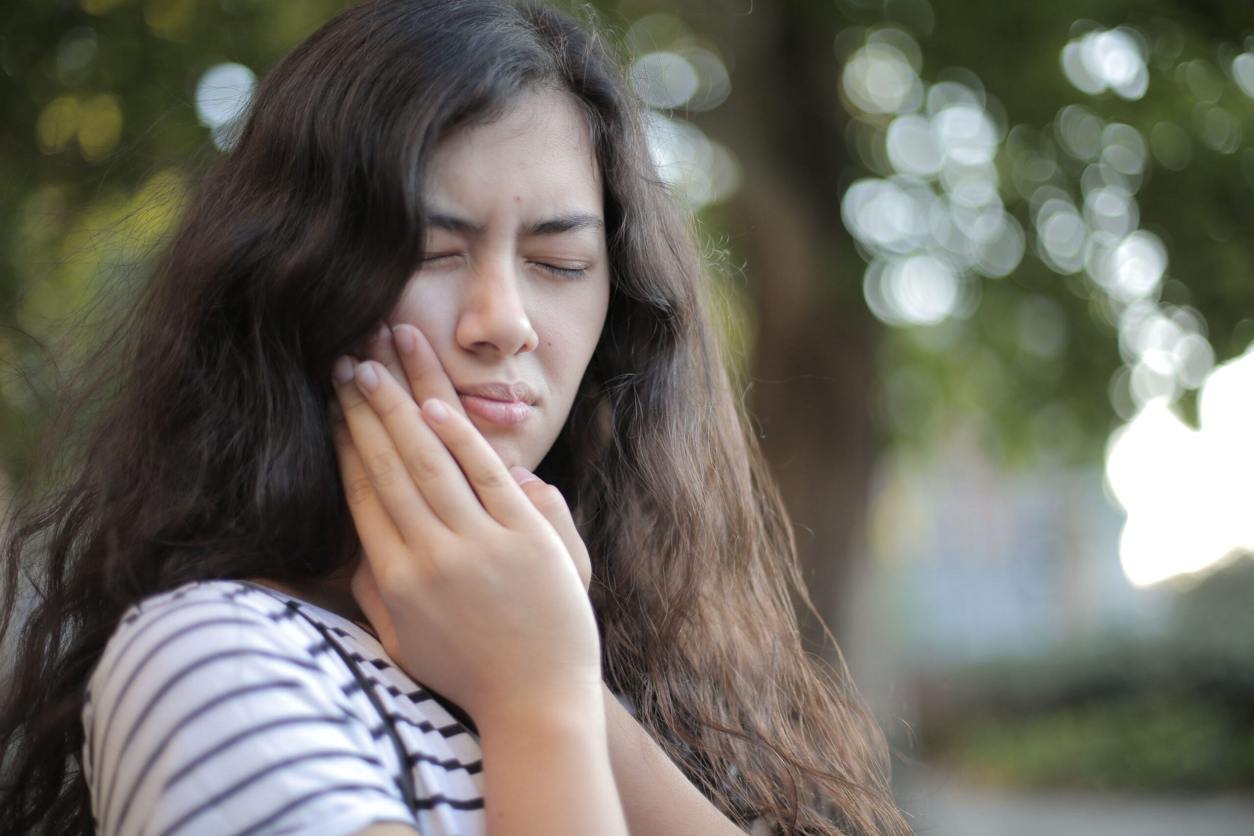 woman holding her jaw in discomfort, illustrating morning jaw pain, teeth grinding, and TMJ symptoms