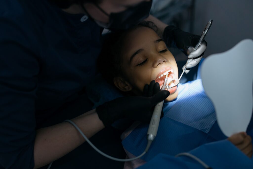 Child receiving a preventive dental examination to assess oral health and possible fluoride treatment needs.